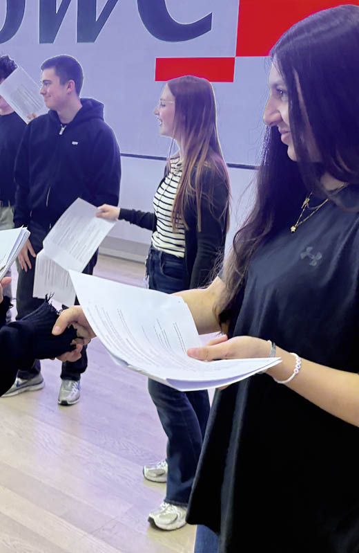Sechs Personen sitzen an einem Tisch in einem modernen Besprechungsraum und arbeiten konzentriert an Unterlagen, w hrend auf einem Bildschirm eine Pr sentation mit farbigen K stchen und Daumen-hoch- und Daumen-runter-Symbolen angezeigt wird. Beschreibung von KI generiert