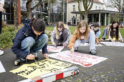 Mehrere Kinder sitzen auf dem Boden im Freien und malen mit Pinseln und Farbe auf gro en Papierb gen, w hrend sie sich auf ihre Arbeit konzentrieren. Beschreibung von KI generiert
